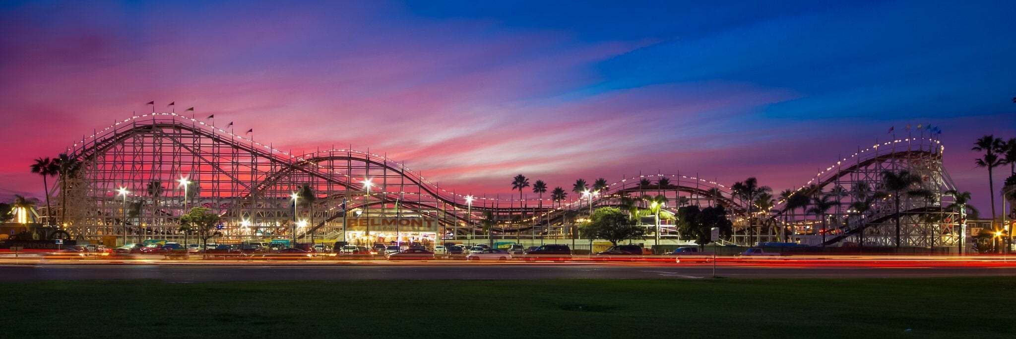 A roller coaster at dusk with a clear sky and lights illuminating the structure.