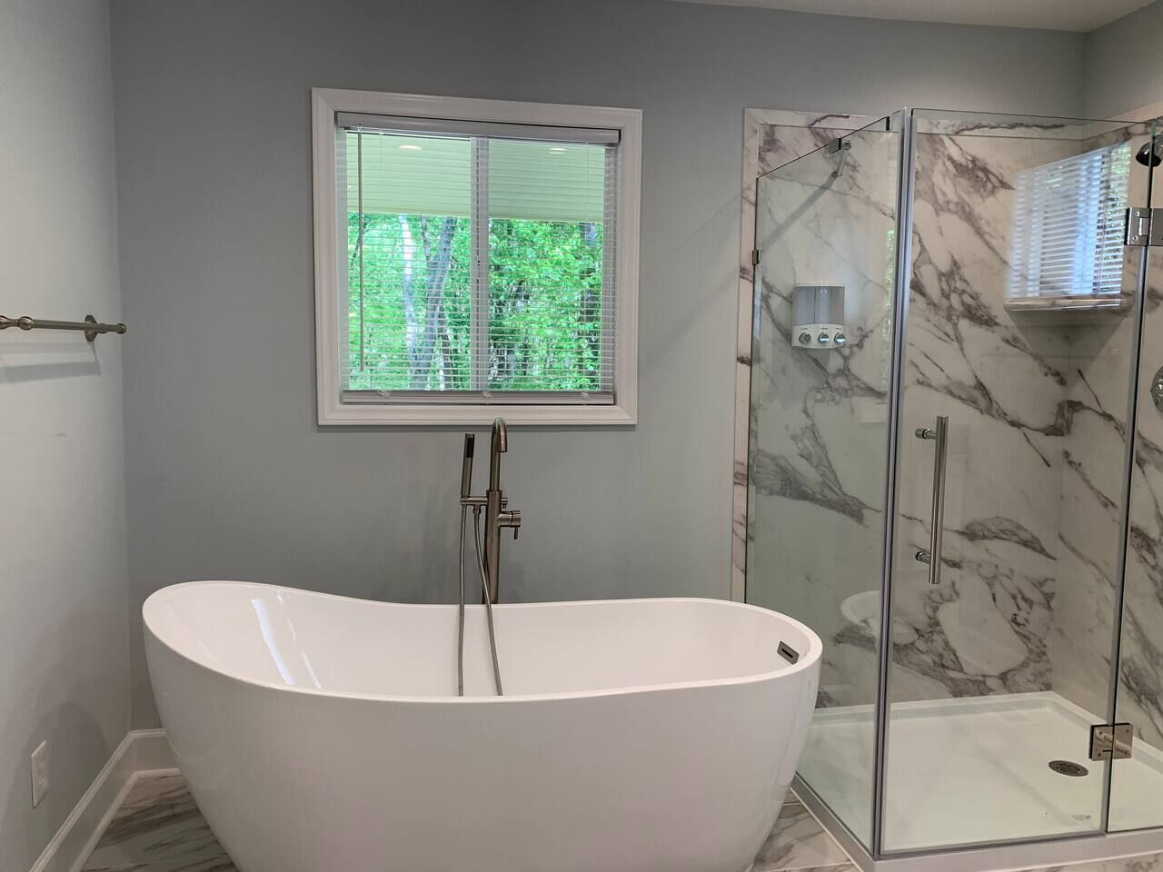 A modern bathroom with a freestanding bathtub, a glass-enclosed shower, and a window with blinds.