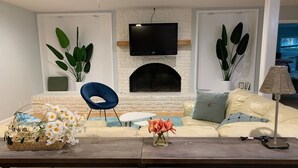 A living room with a sofa, a coffee table, a TV mounted above a fireplace, and a plant. - Ranch Home Retreat on 4 Acre Land near UNC/Duke (Chapel Hill)