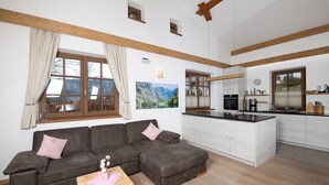 A modern living room with a sofa, a small table, and a kitchen area with a stove and cabinets.