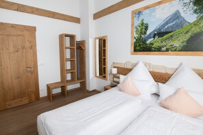 Une chambre à coucher avec un lit en bois, une armoire en bois, un banc et un tableau représentant un paysage de montagne.