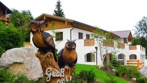 A building with a white facade, wooden balconies, and a large rock with owl sculptures.