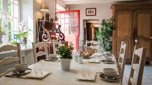 Un comedor con una mesa dispuesta para dos personas, sillas, una puerta roja y diversas plantas.