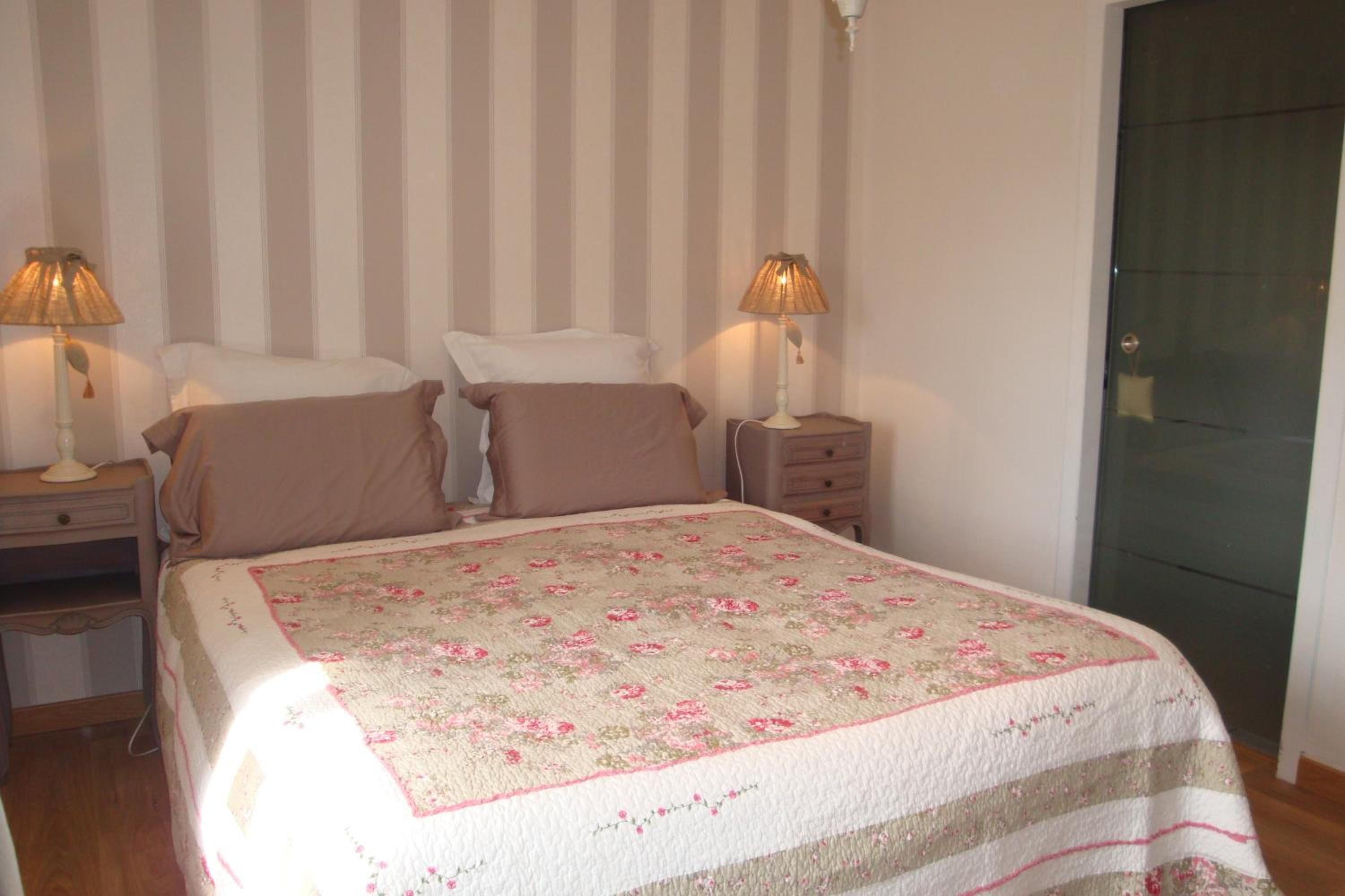 Une chambre à coucher avec un lit, deux tables de chevet avec des lampes, une commode et un mur à rayures.