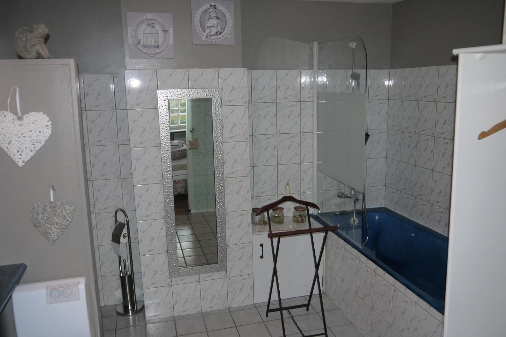 Ein Badezimmer mit Badewanne, Dusche und Toilette. An der Wand befinden sich dekorative Elemente, darunter eine herzförmige Dekoration und ein gerahmtes Bild.