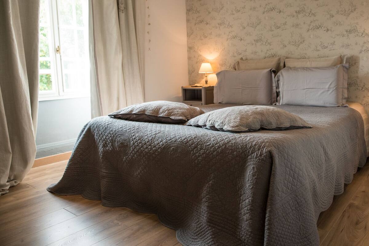 Un dormitorio con una cama grande, dos mesitas de noche, una ventana con cortinas y una lámpara en cada mesita.