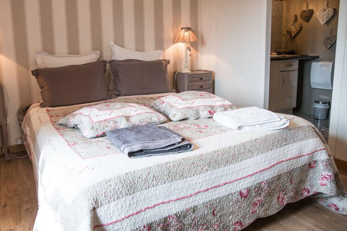 Una cama bien tendida con una colcha floral, dos lámparas de noche y una mesita de noche con lámpara.