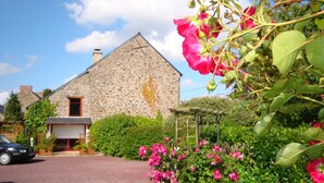 Un edificio de piedra con puerta roja, rodeado de abundante vegetación y flores rosadas.