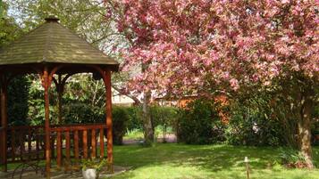 A gazebo in a garden with blooming pink flowers and green grass.
