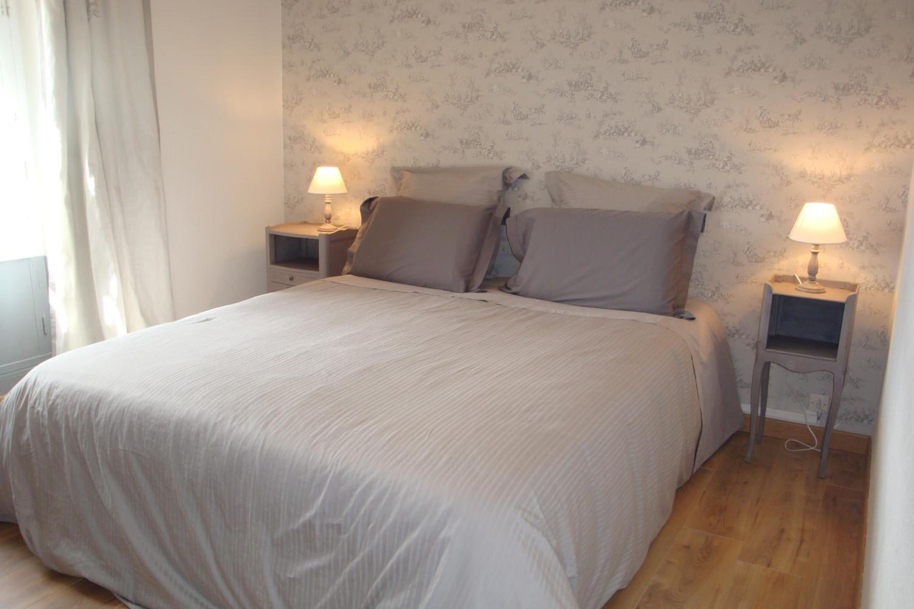 A neatly made bed with a light-colored duvet, two bedside tables with lamps, and a floral wallpaper pattern on the walls.