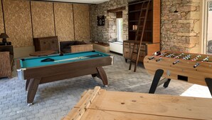 Een kamer met een pooltafel, tafelvoetbal en een stenen muur.
