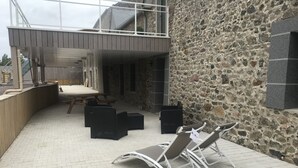 Een buitenzitplaats met lounge stoelen en een tafel, een stenen muur en een gebouw met balkon.