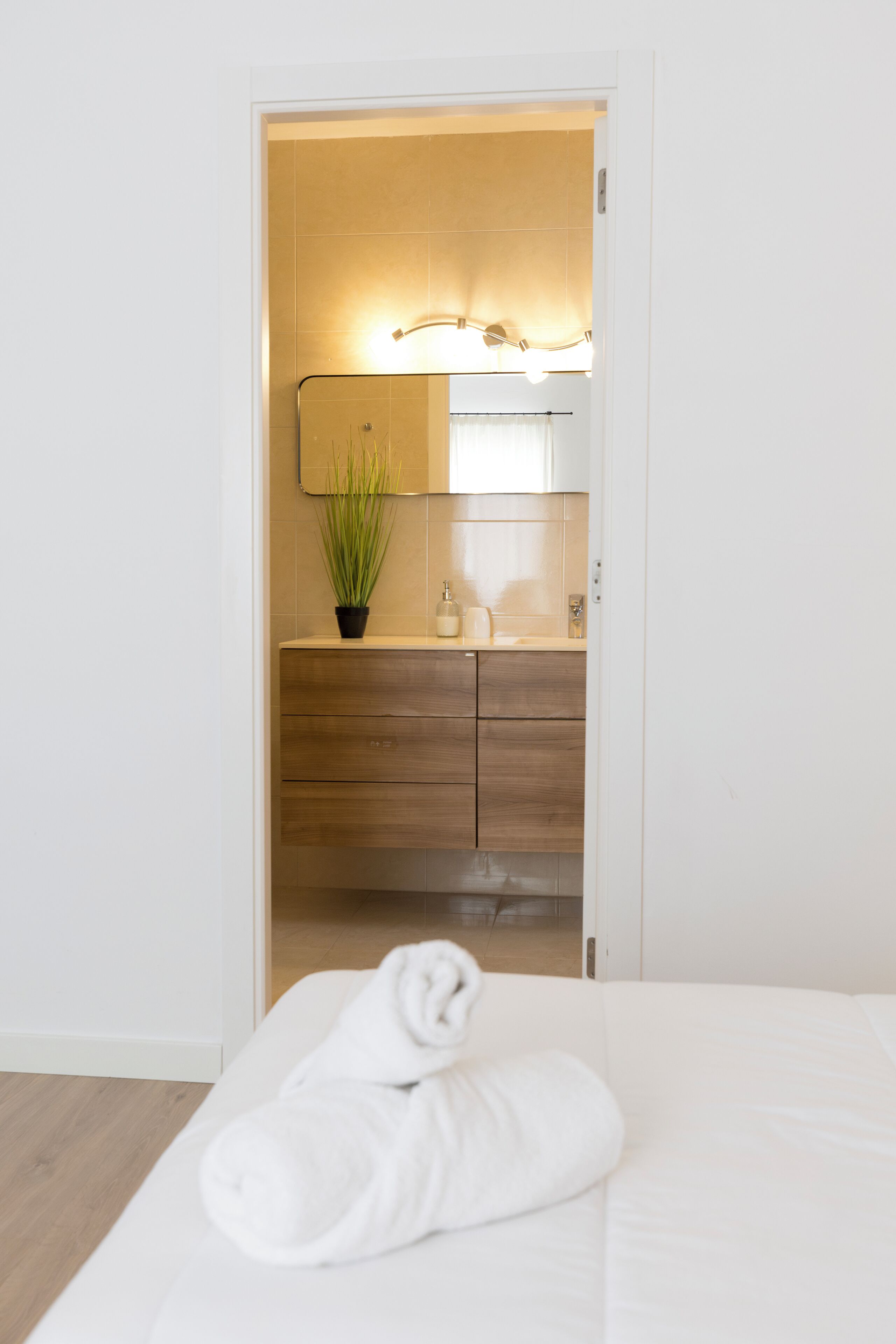 A hotel room with a bed, a bathroom with a mirror, a sink, and a potted plant.
