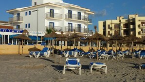 Un hotel frente a la playa con varios balcones, tumbonas y sombrillas de paja.