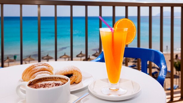 Una mesa con una bebida, pasteles y una taza de café en un balcón con vistas al mar.