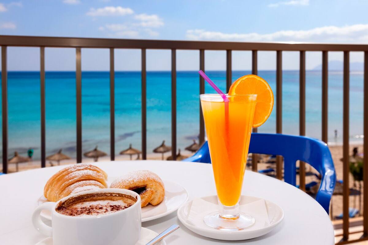 Una mesa con una bebida, pasteles y una taza de café en un balcón con vistas al mar.