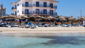 Un hotel frente a la playa con aguas azules cristalinas, una playa de arena y sombrillas.