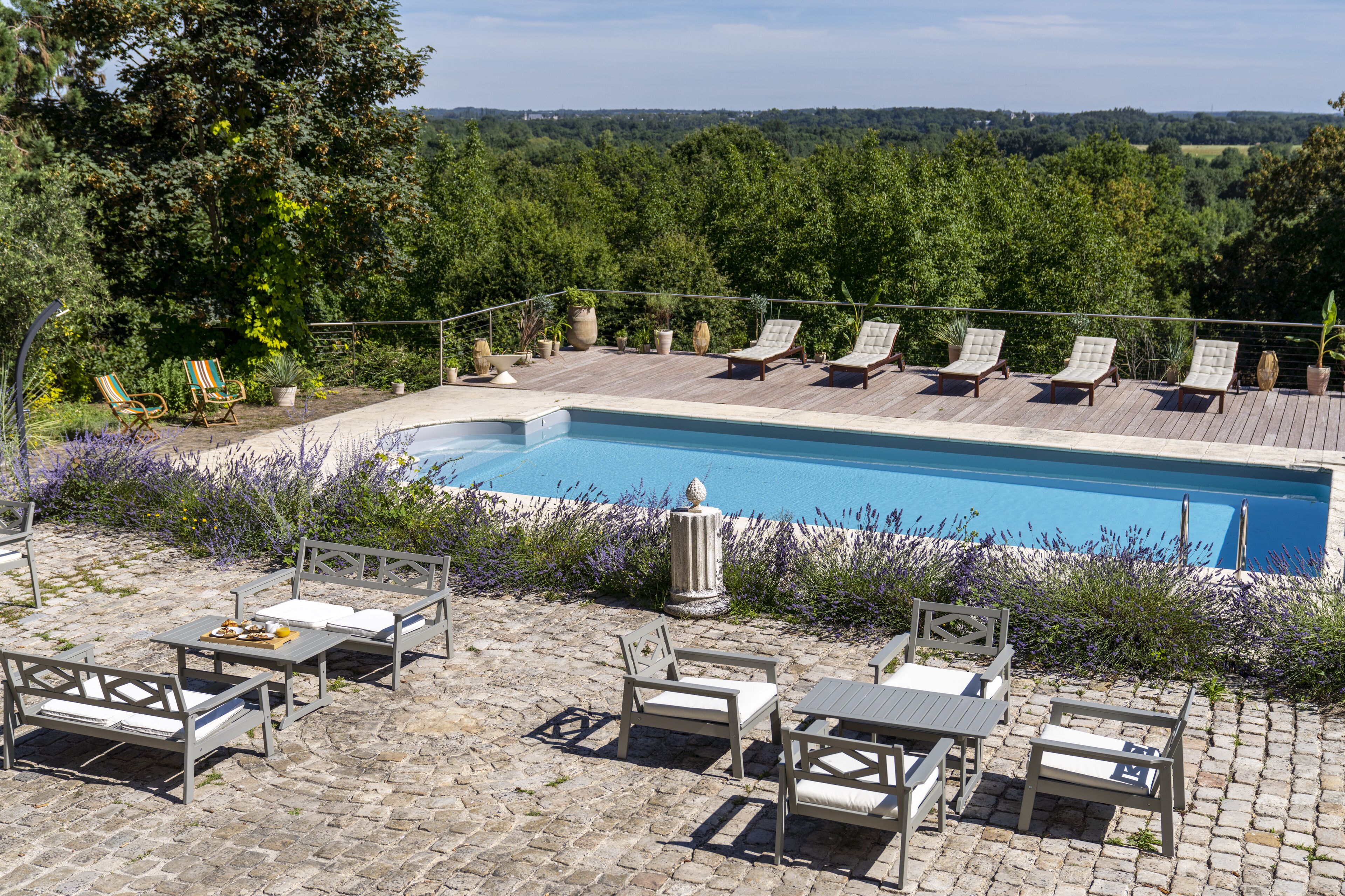 Zona junto a la piscina con sillones de descanso y una mesa, rodeada de follaje y vistas al paisaje.