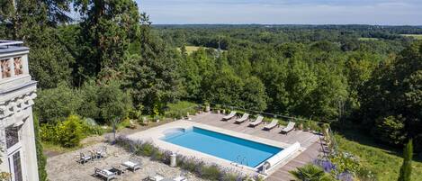Una piscina en la azotea con sillones de descanso y zona de comedor, rodeada de abundante vegetación y vistas al bosque.