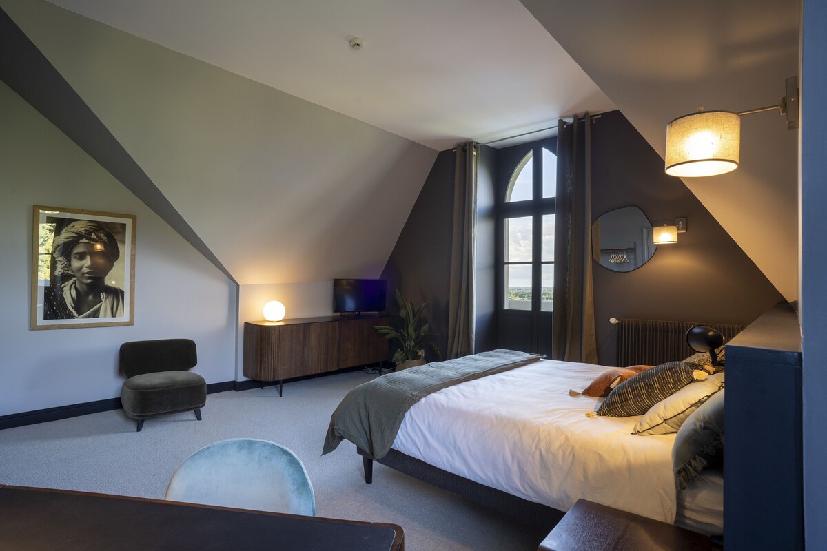 Un dormitorio moderno con una cama grande, un escritorio, una silla, un televisor y un ventanal amplio.