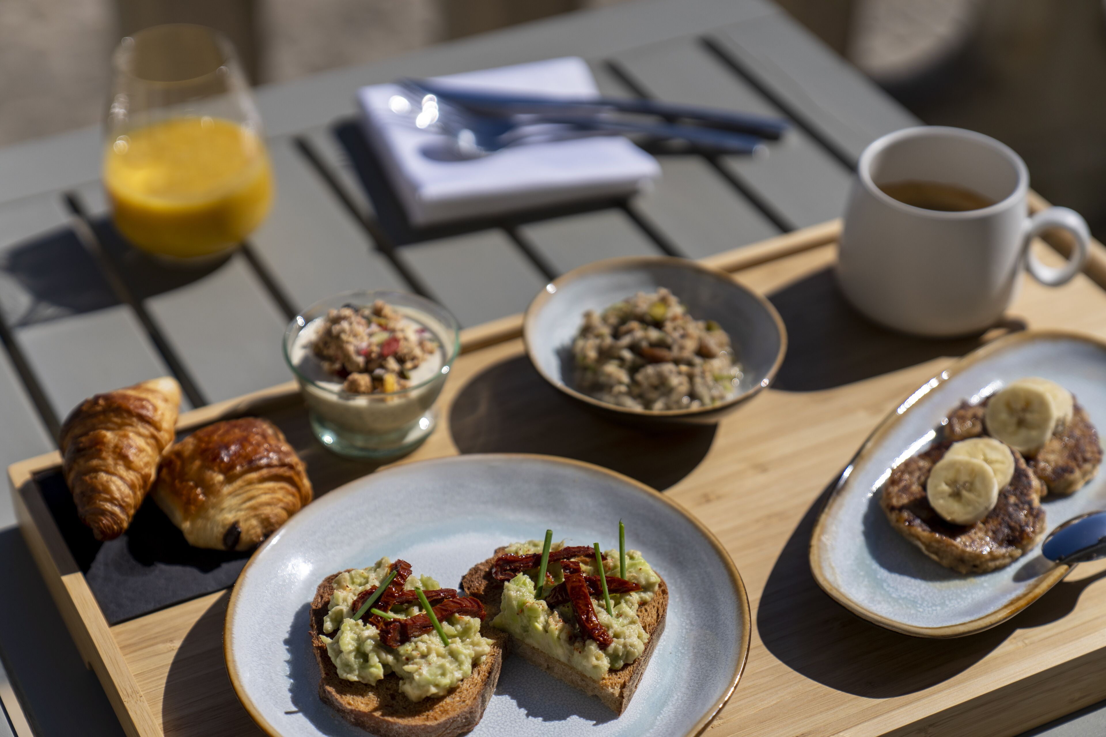 Een ontbijfwagen met croissants, toast met avocado en zongedroogde tomaten, een kom cornflakes, een kop koffie en een glas jus d'orange.