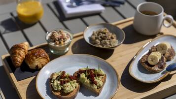 Een ontbijfwagen met croissants, toast met avocado en zongedroogde tomaten, een kom cornflakes, een kop koffie en een glas jus d'orange.