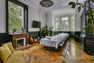 Un comedor con una mesa larga dispuesta para una comida, una chimenea y un ventanal con vistas a árboles.