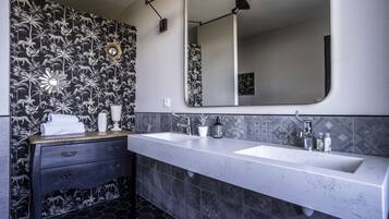 Een badkamer met behang in zwart-wit bloemenmotief, twee wasbakken, een spiegel en een wastafelmeubel met lades.