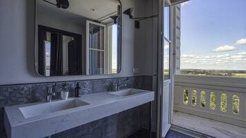 A modern bathroom with two sinks, a large mirror, and a view of the countryside through a balcony.