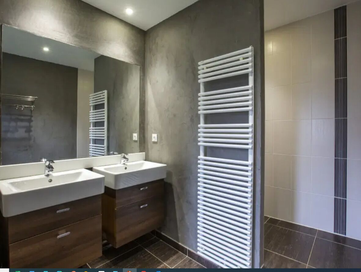 A modern bathroom with two sinks, a large mirror, and a towel rack.
