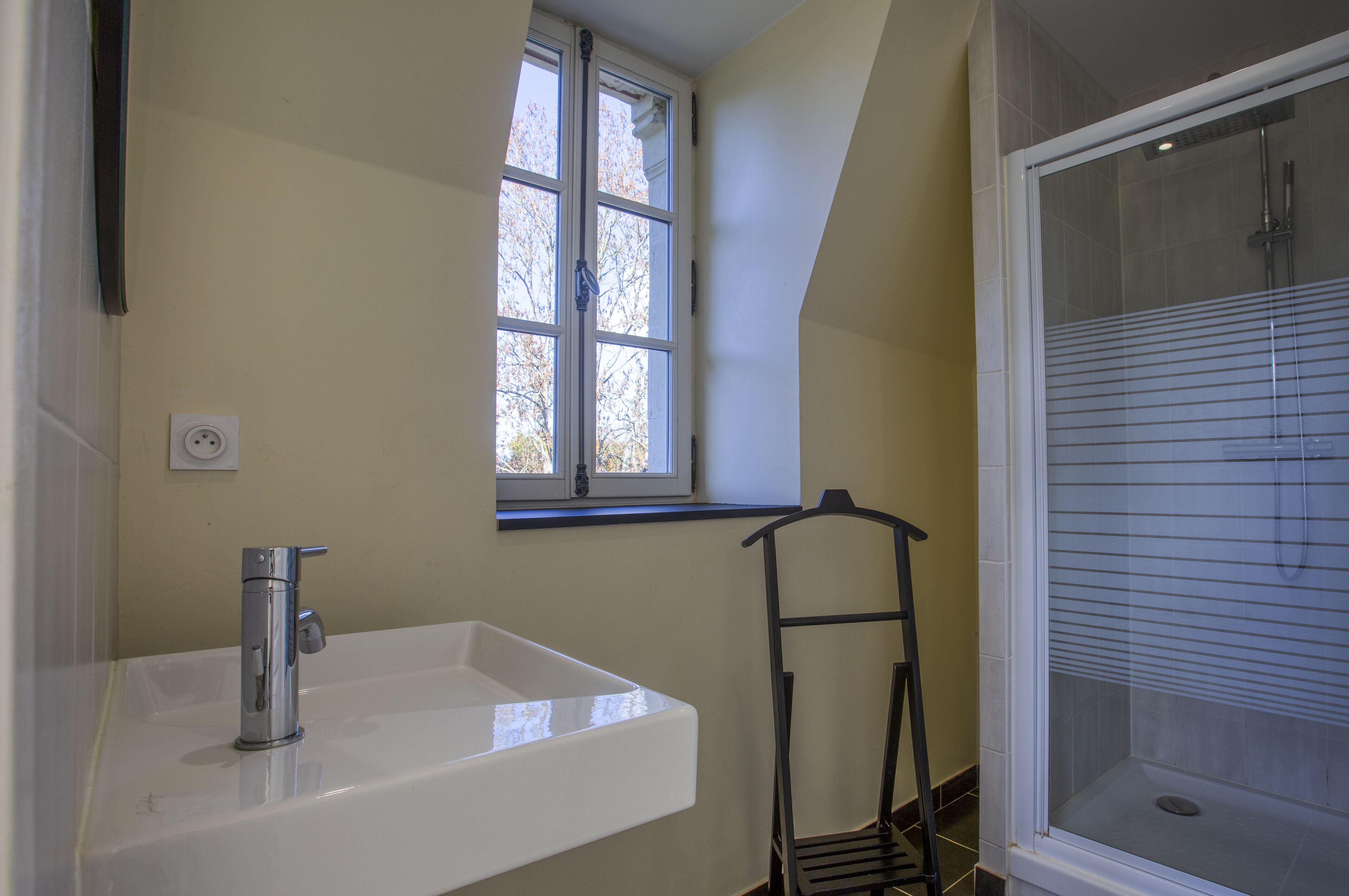 A bathroom with a white sink, a window, and a shower area.