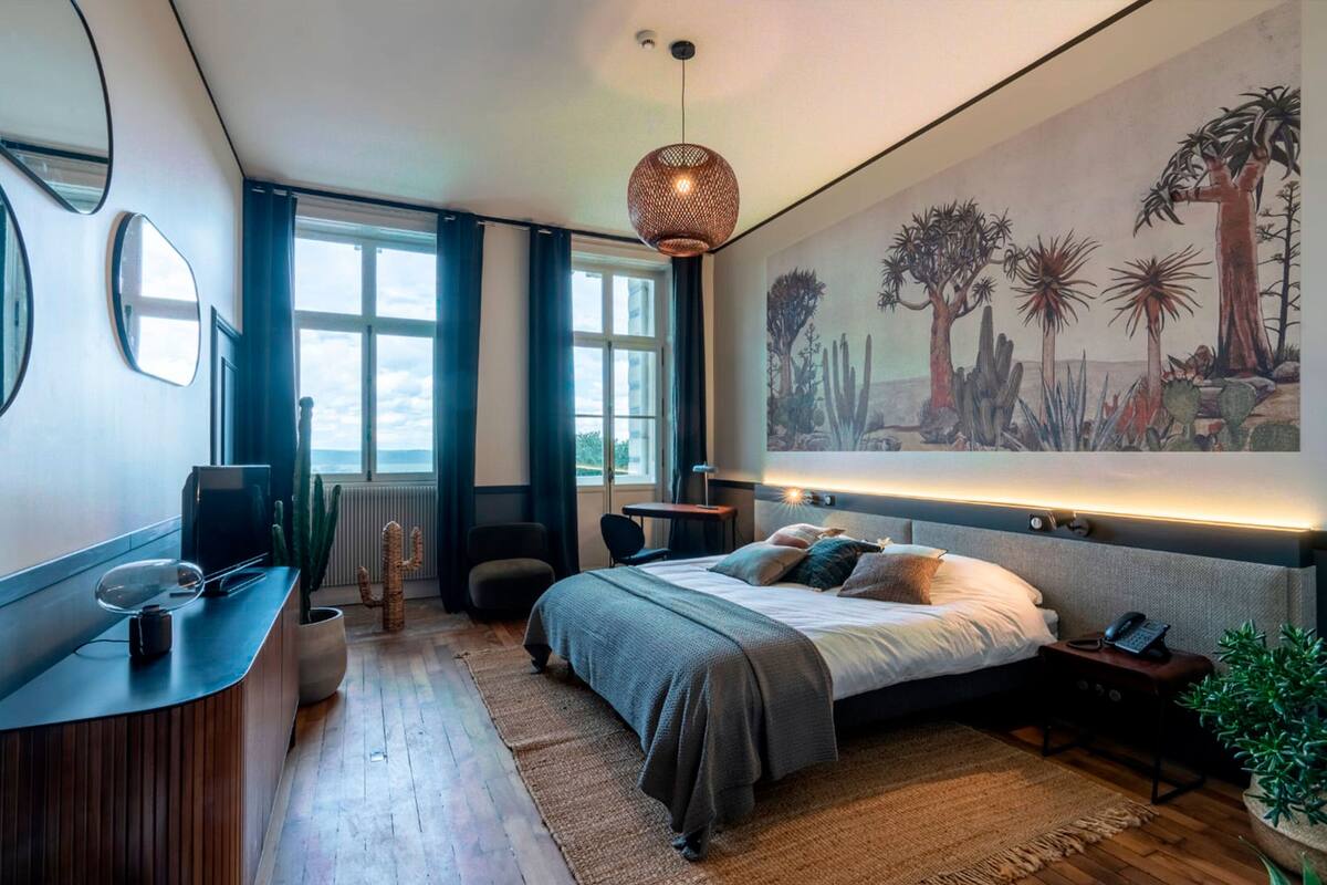 A modern bedroom with a large bed, a desk, a chair, and a large window.