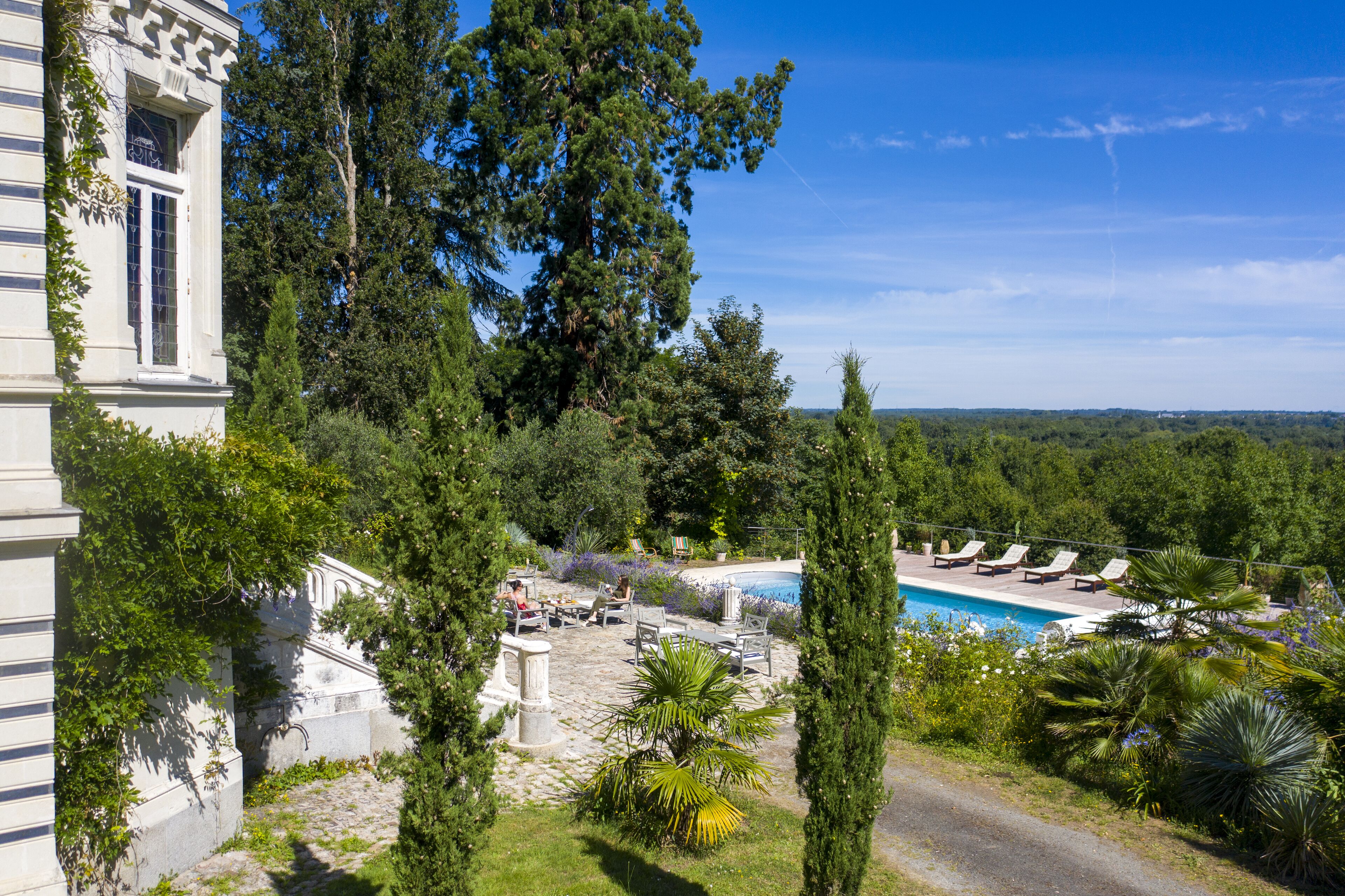 Un área de piscina con sillas de descanso y vistas a un paisaje boscoso.
