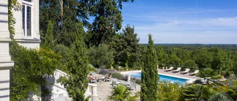 Un área de piscina con sillas de descanso y vistas a un paisaje boscoso.