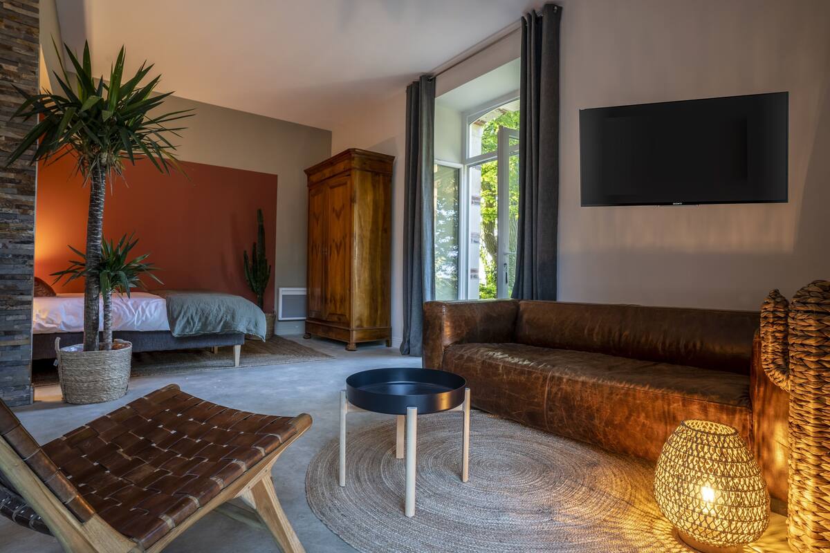 A modern living room with a sofa, a coffee table, a TV mounted on the wall, and a large window with curtains.