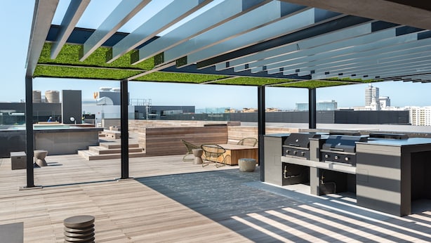 A rooftop terrace with a modern outdoor kitchen, seating area, and a view of the city skyline. - Brand New Modern De Waterkant Apartment (Cape Town)