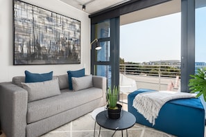 Relax in this stylish living room with a sofa, coffee table, and potted plant, leading to a balcony with a seating area overlooking the city.