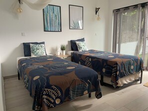 A bedroom with two beds, a nightstand, a potted plant, and artwork on the wall.