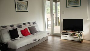 A modern living room with a sofa, a flat-screen TV, and a sliding glass door leading to an outdoor area. - Quiet apartment with terrace for 6 people, 3 bedrooms. (Gérardmer)
