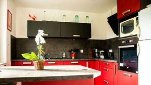 A modern kitchen with red cabinets, a marble countertop, and a microwave. - Quiet apartment with terrace for 6 people, 3 bedrooms. (Gérardmer)
