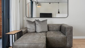 A modern living room with a grey sectional sofa, a small wooden side table, and a large mirror on the wall.