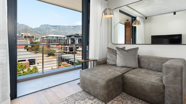 A modern living room with a large window, a grey sofa, and a flat-screen TV.