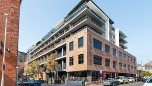 A multi-story building with a brick facade, multiple balconies, and a ground-level cafe.