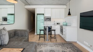 A modern kitchen with white cabinets, a grey sofa, and a bar stool.