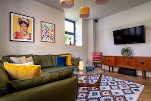A modern living room with a green sofa, a patterned rug, a glass coffee table, and a flat-screen TV mounted on the wall. - Two Guns (Kingswear)