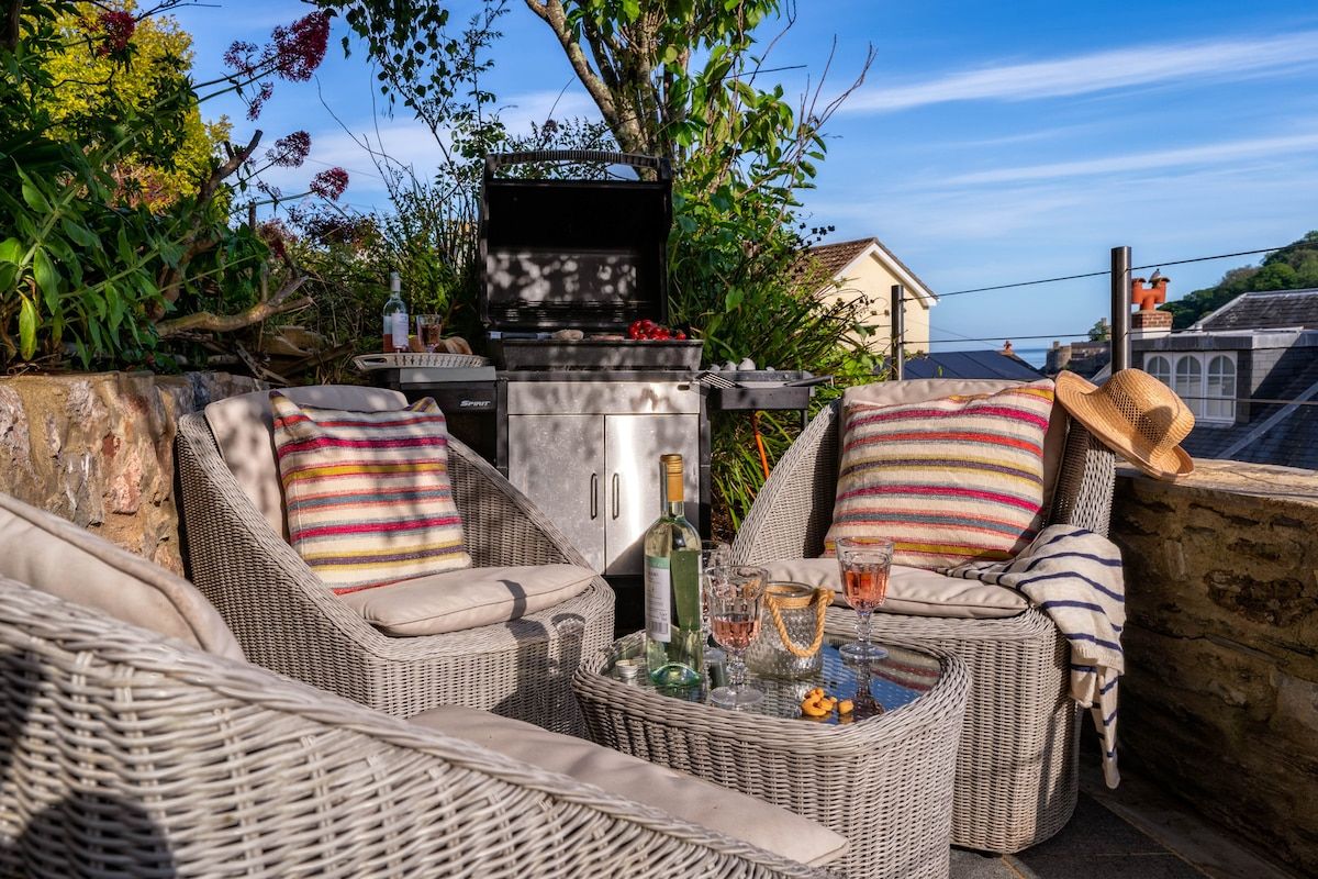 An outdoor seating area with wicker furniture, a grill, and a view of the sea.