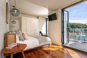 A bedroom with a bed, a bedside table, a chair, a TV, and a balcony with a view. - Two Guns (Kingswear)