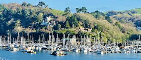 A marina with numerous boats docked, surrounded by hills and a few buildings in the background.