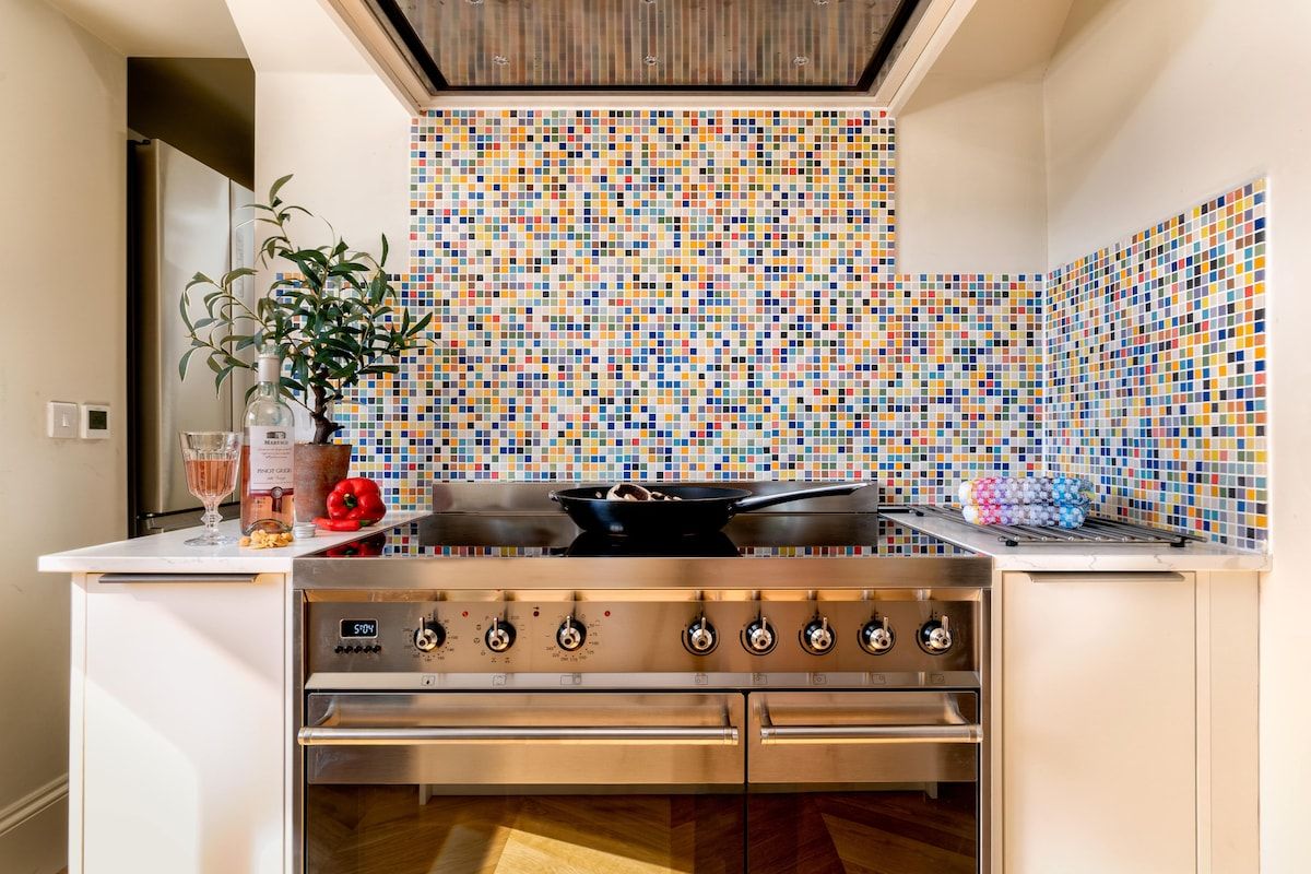 Een keuken met een moderne kookplaat, een kleurrijke mozaïektegel achterwand en een bloempot.