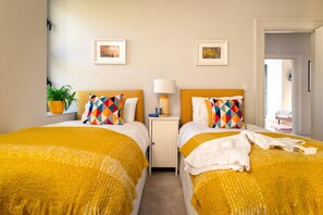 A hotel room with two beds, a nightstand with a lamp, and artwork on the walls.